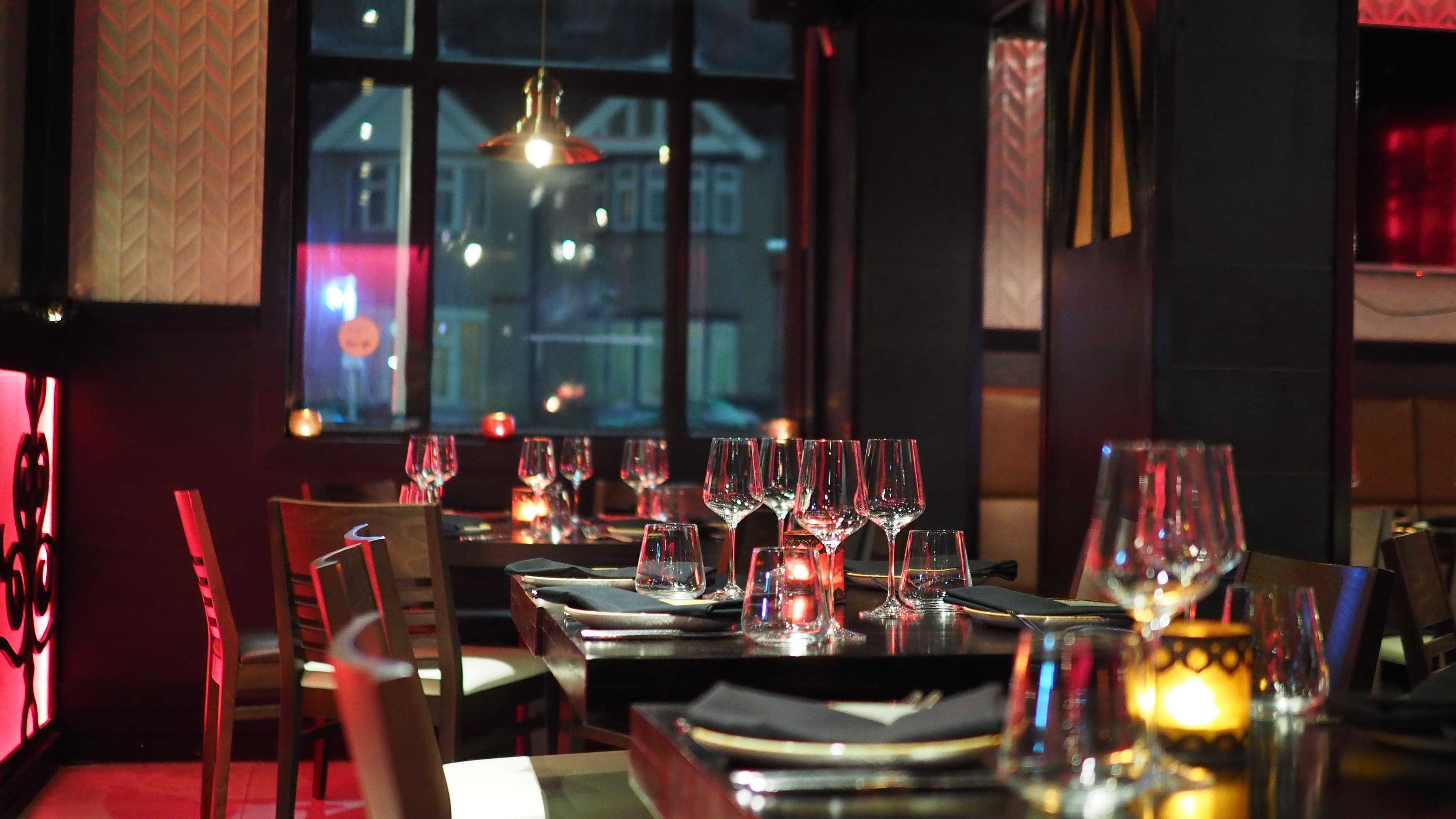 Dimly lit restaurant with tables set for dinner, wine glasses, and warm red ambient lighting.
