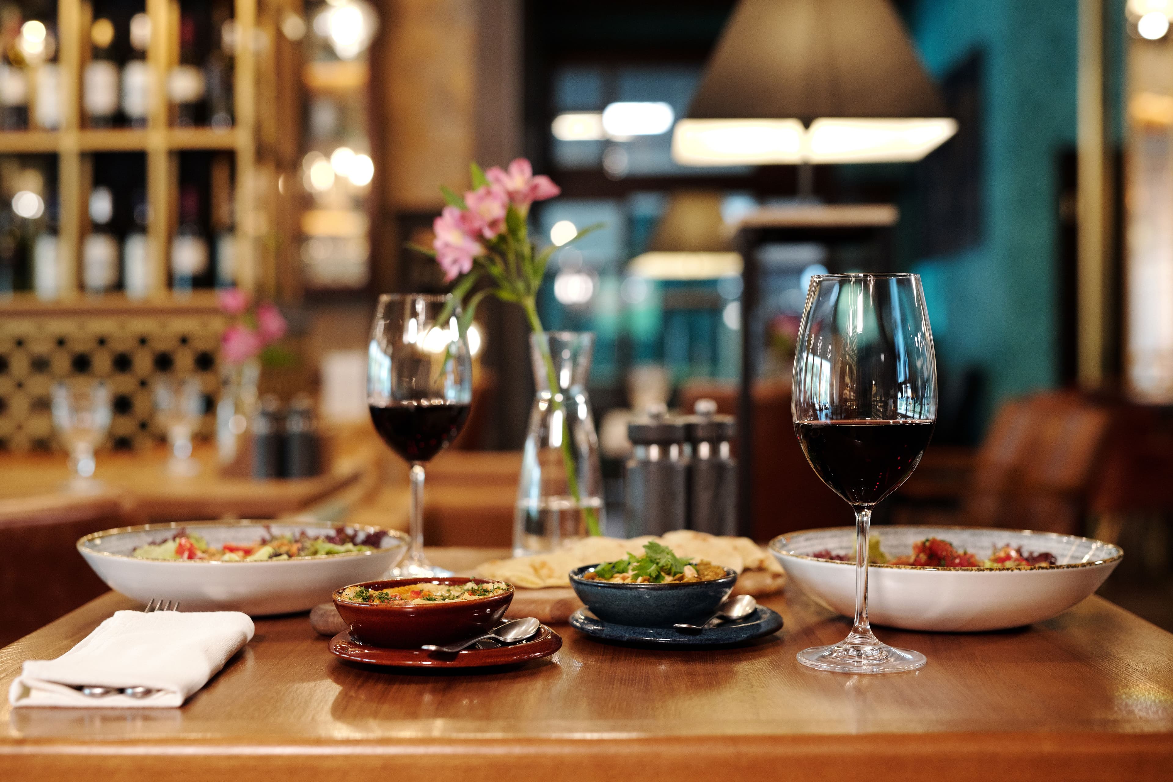 Red wine and gourmet dishes on a wooden table in a dimly lit, elegant restaurant.